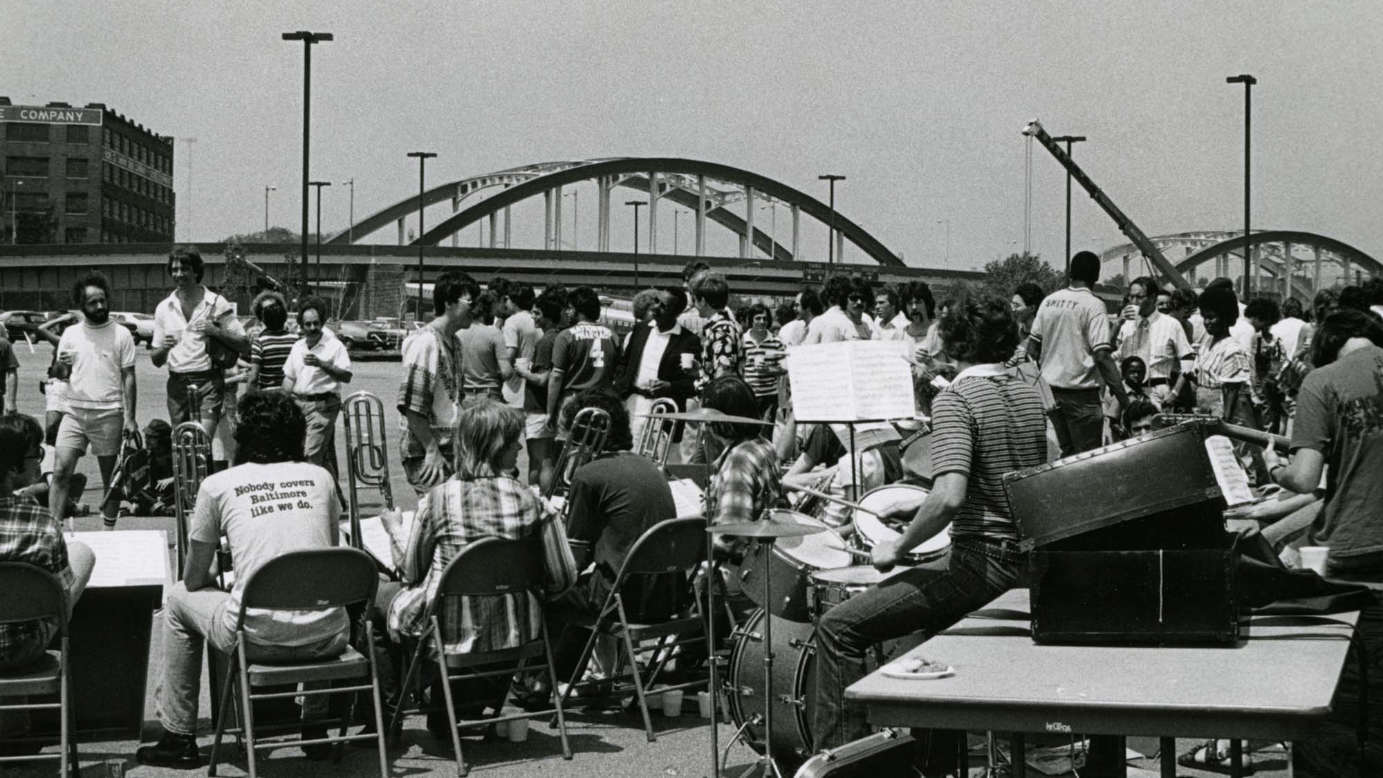 A crowd fills the block with a bridge in the background.